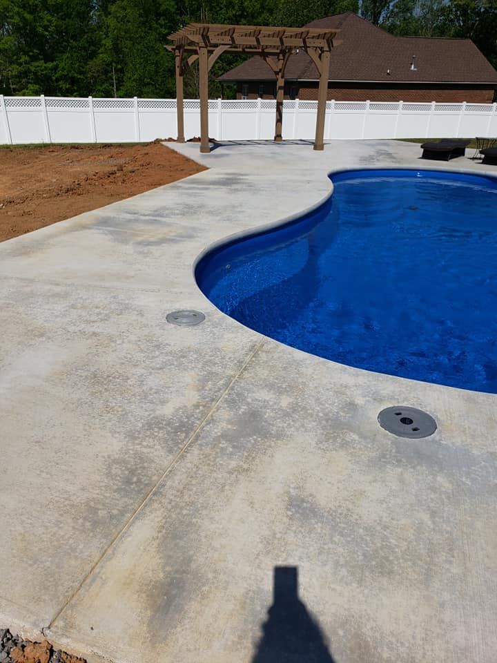 Backyard swimming pool with concrete deck and wooden pergola beside a white fence
