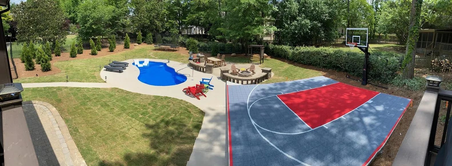 Backyard with blue play area, sandbox, red-and-blue court, and a fire pit surrounded by trees