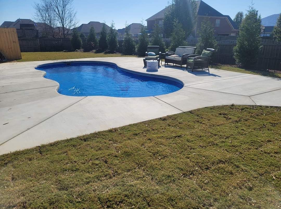 Backyard swimming pool with blue cover, concrete deck, chairs, and a grassy lawn in sunlight