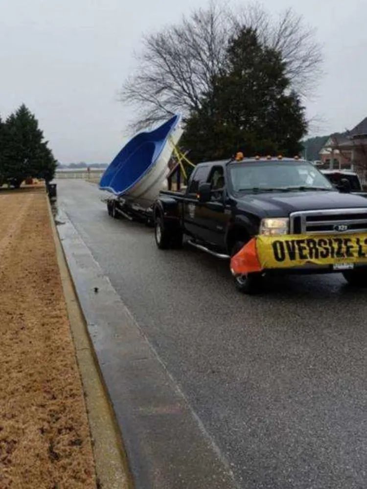 Tow truck hauling a boat on a wet roadside, with an oversized load banner on the front.