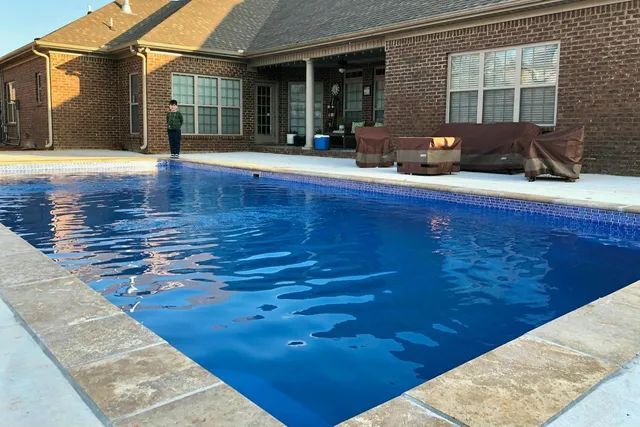 Backyard patio with a rectangular swimming pool beside a brick house and outdoor seating