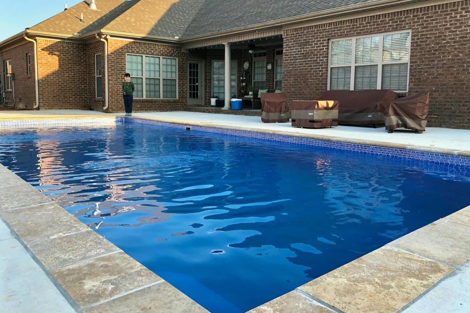 Backyard swimming pool beside a brick house with patio seating and a covered porch