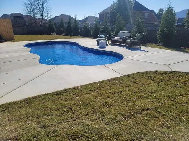 Backyard with a kidney-shaped blue pool, concrete patio, lounge chairs, and lawn in sunlight