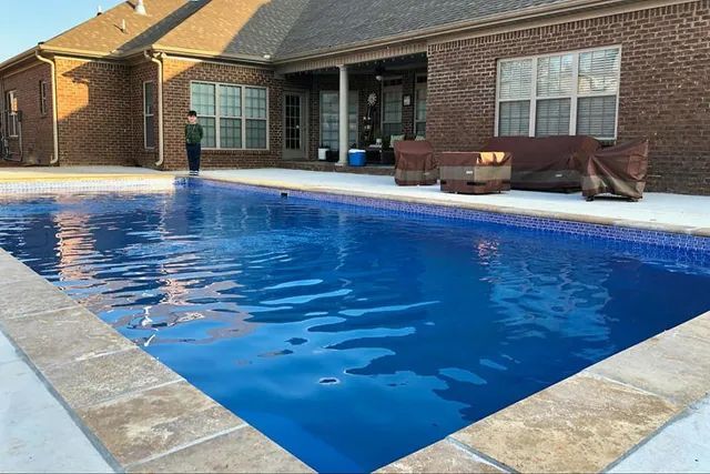 Brick patio with a clear blue swimming pool beside a house, with lounge chairs and a covered seating area