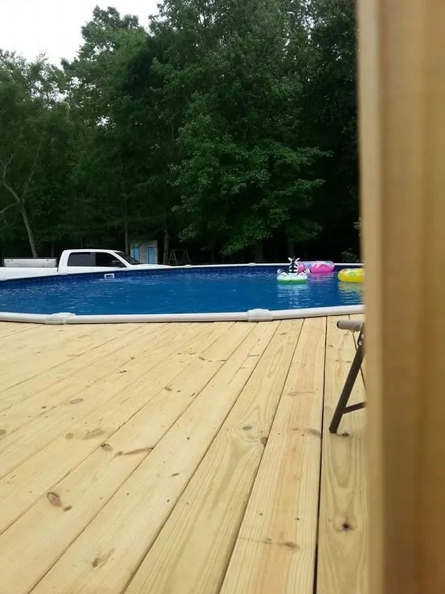 Wooden deck beside an above-ground pool with colorful floaties and trees in the background