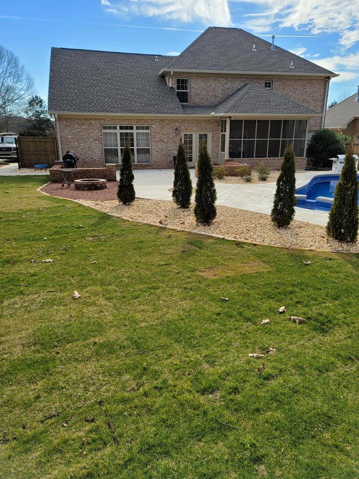 Backyard patio with brick house, lawn, gravel beds, and a small blue pool under a cloudy sky