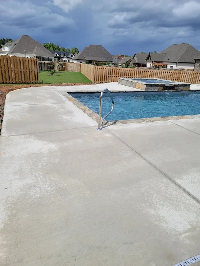 Swimming pool with blue water, concrete deck, and fenced backyard with thatched-roof houses in the distance
