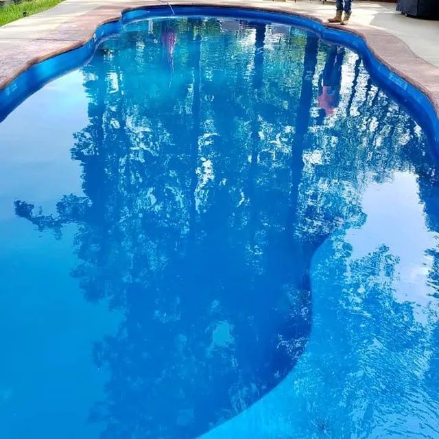 Blue swimming pool reflecting trees and sky, with a stone edge and curved shape