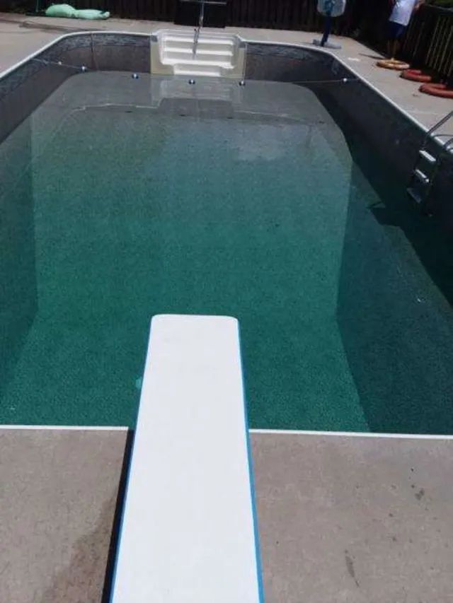 Backyard swimming pool with a white diving board and steps at the far end