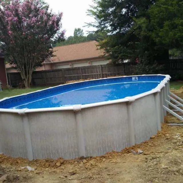 Round above-ground pool in a backyard with a blue liner and white wall, beside a house and trees