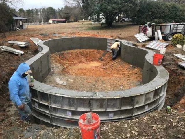 Workers installing a large circular concrete foundation on a muddy construction site