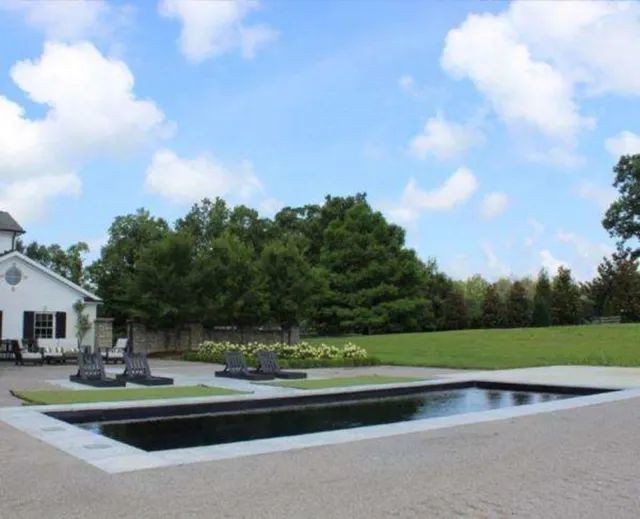 Modern backyard with a rectangular pool, patio seating, lawn, and a white house under a blue sky