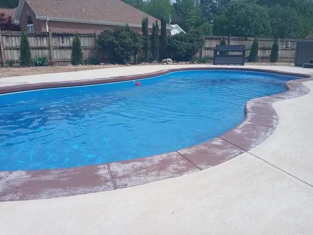 Backyard swimming pool with blue water, concrete deck, and a bench in the background
