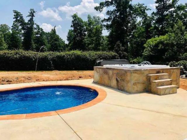 Backyard pool with blue water, tan patio, and built-in stone spa under trees