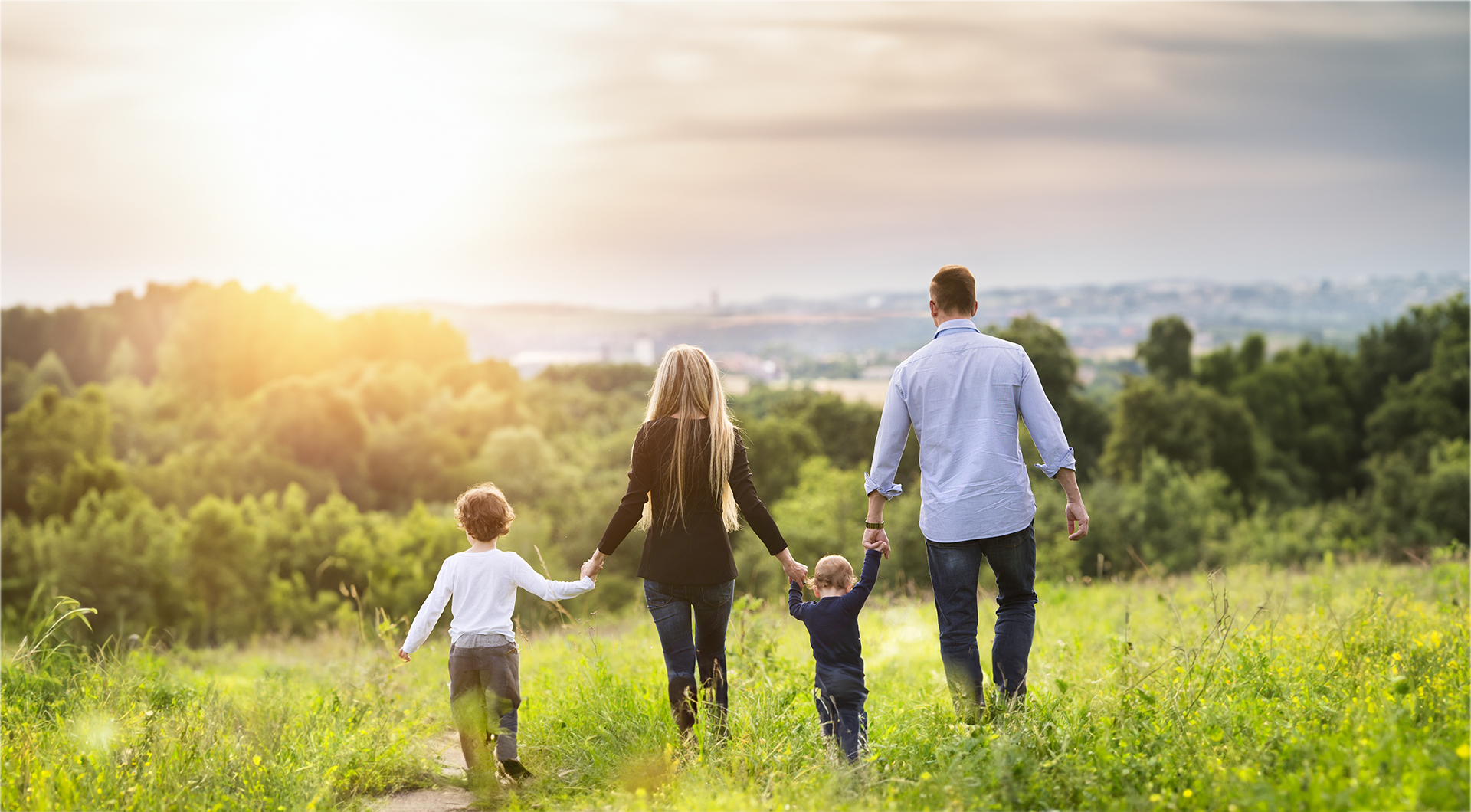 A family is walking through a grassy field holding hands.