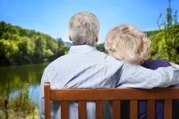 a man and woman sit on a bench looking at a lake