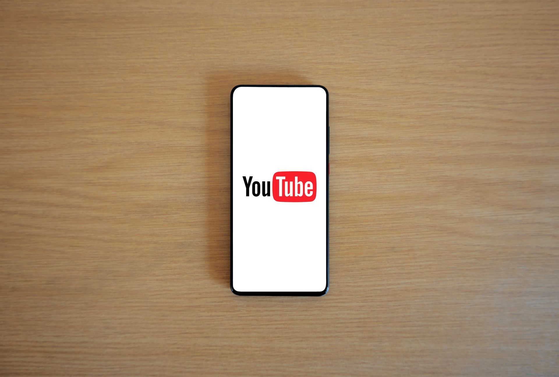 A cell phone with the youtube logo on the screen is sitting on a wooden table.