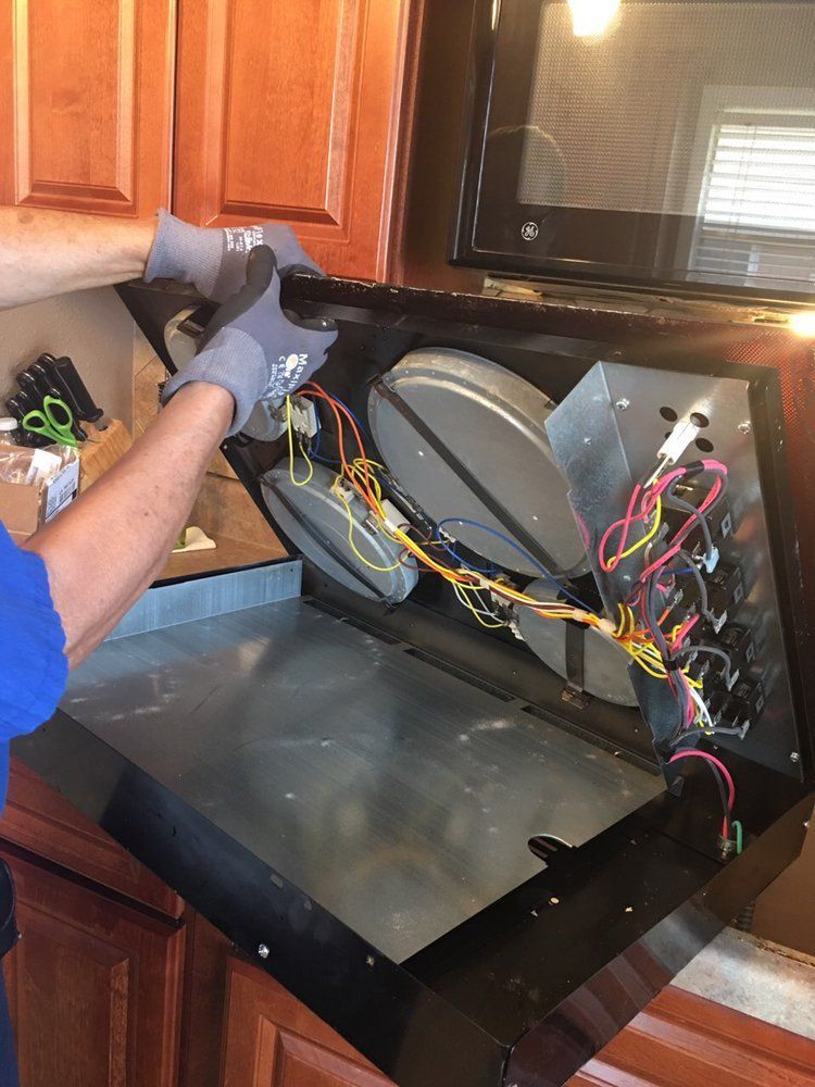 A man is working on a microwave in a kitchen.