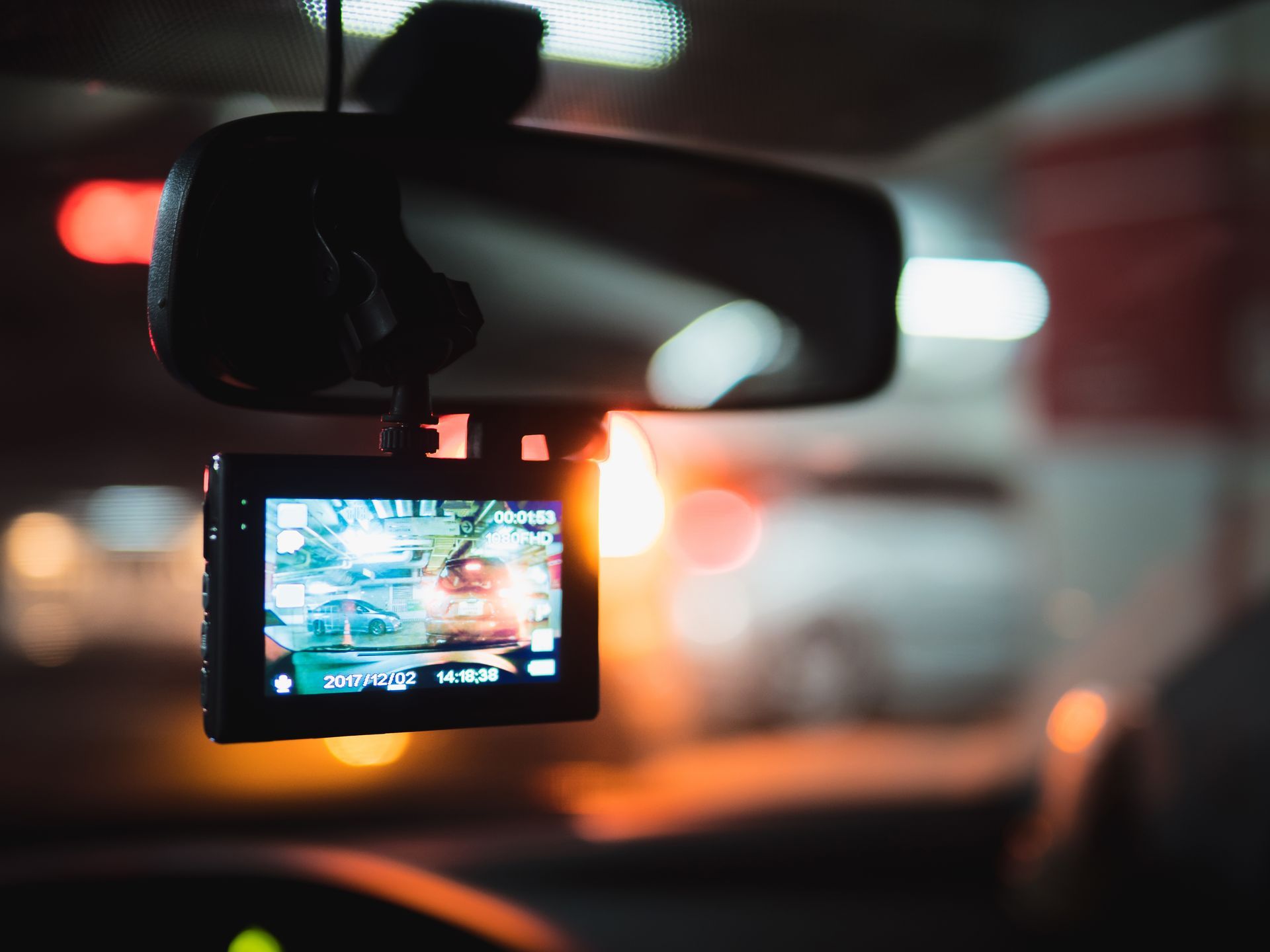 A dash cam is hanging from the rear view mirror of a car.