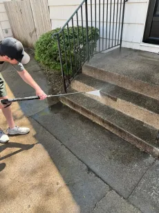 A person cleans a dirty gutter with a hose, near a rooftop.