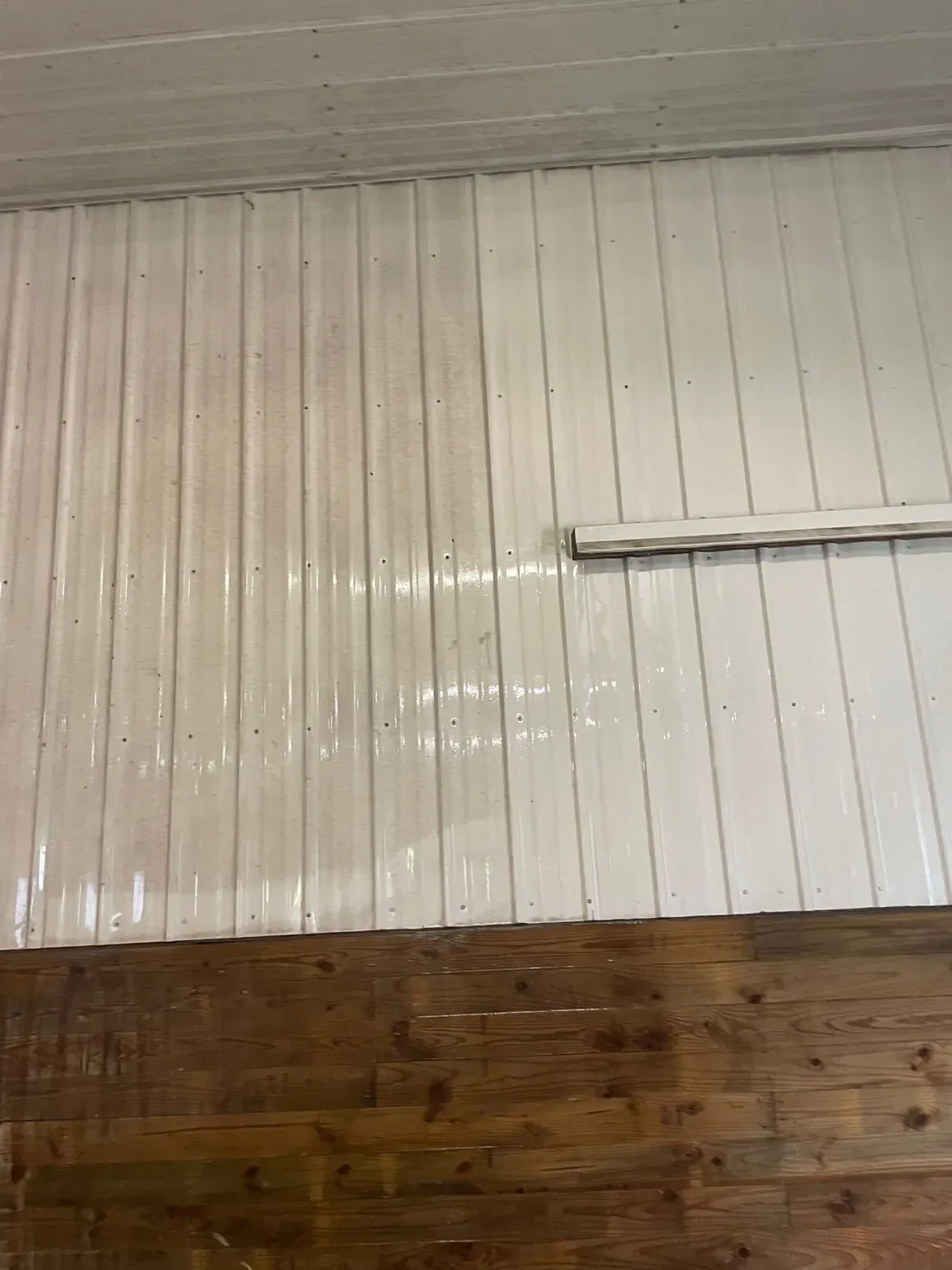 White corrugated metal wall above brown wooden planks.