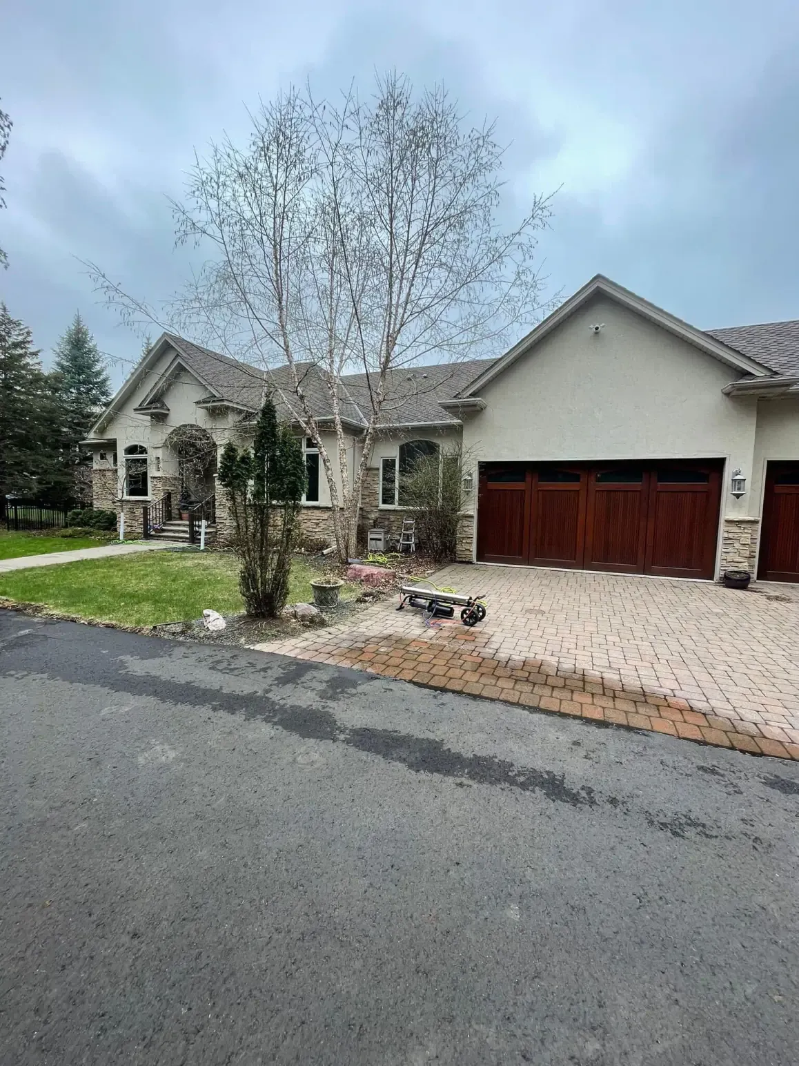 House with stone facade, brick driveway, and brown garage doors on a cloudy day.