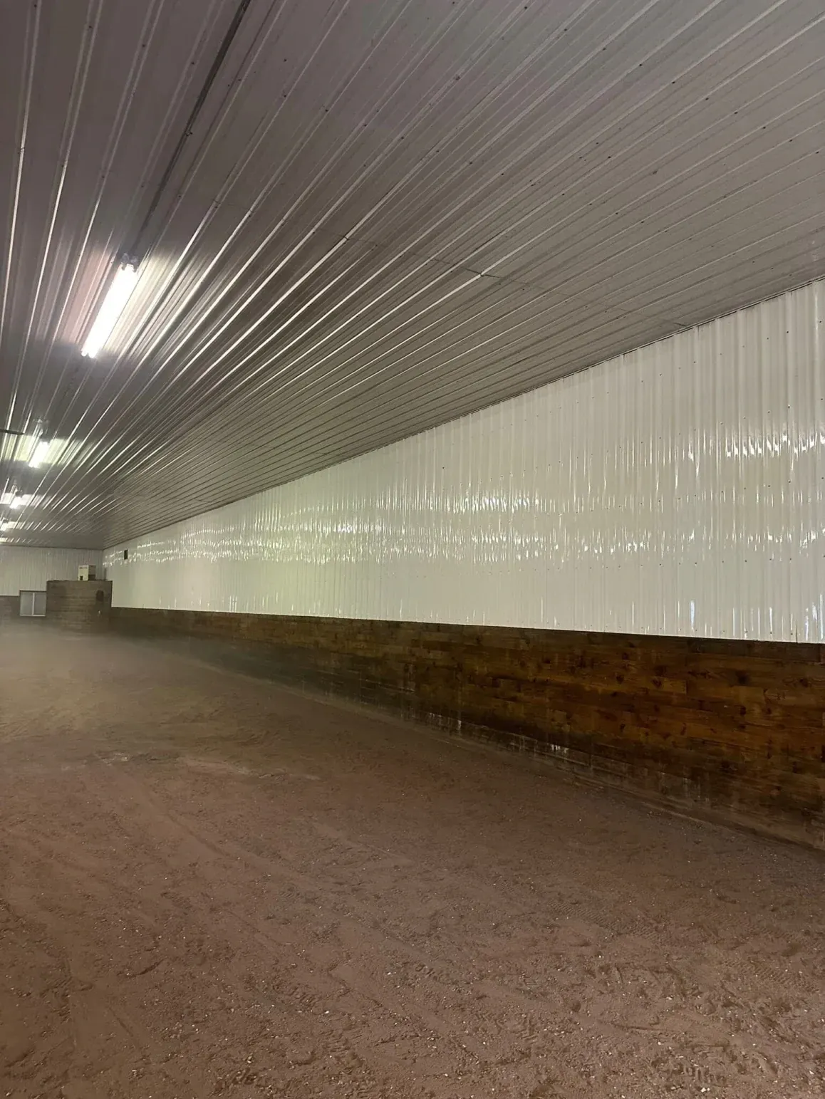 Indoor riding arena, brown dirt floor, white walls and ceiling.