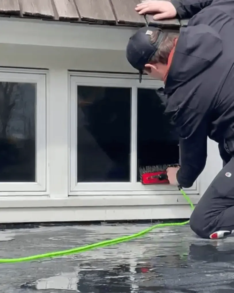 Person cleaning a window with a brush. Green hose. Outdoors.