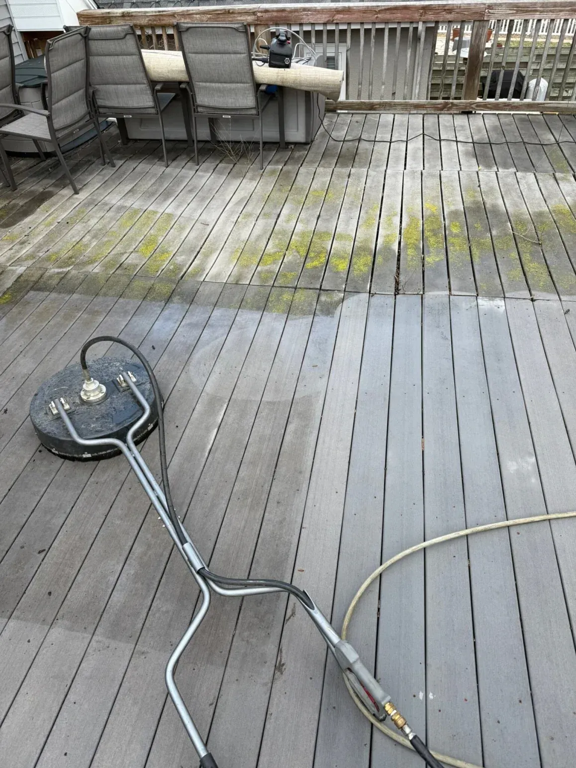 A person pressure washing a wooden deck with a cleaning tool, showing wet and cleaned sections.