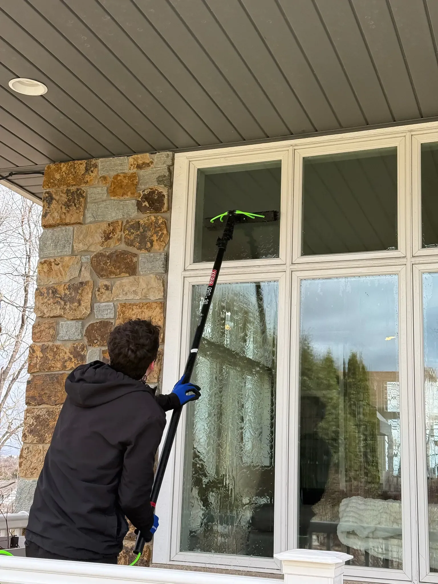Person washing a window with a long-handled brush on a house's exterior.