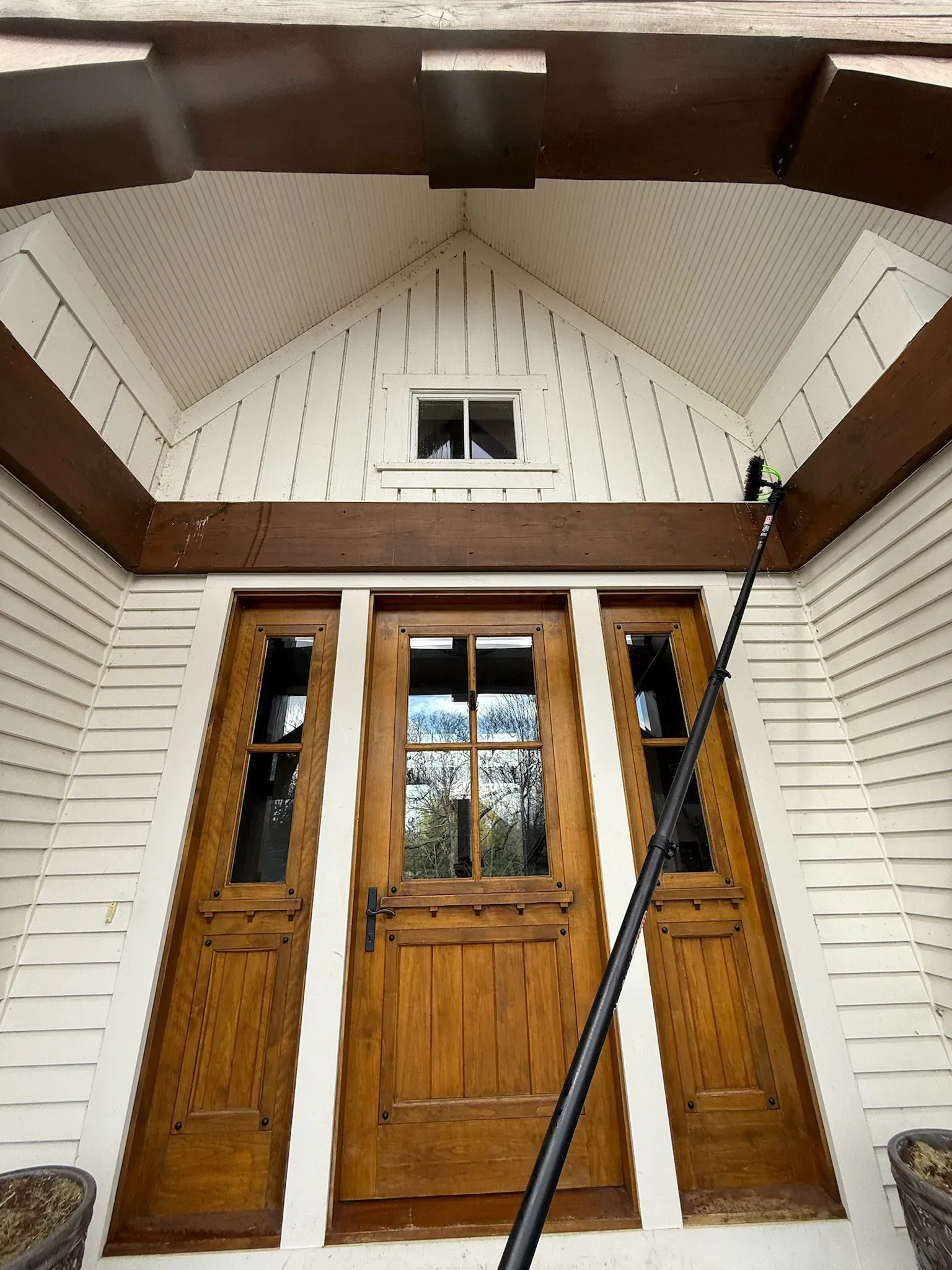 Wooden door and sidelights on a white house, arched entry with brown trim, cleaning pole visible.