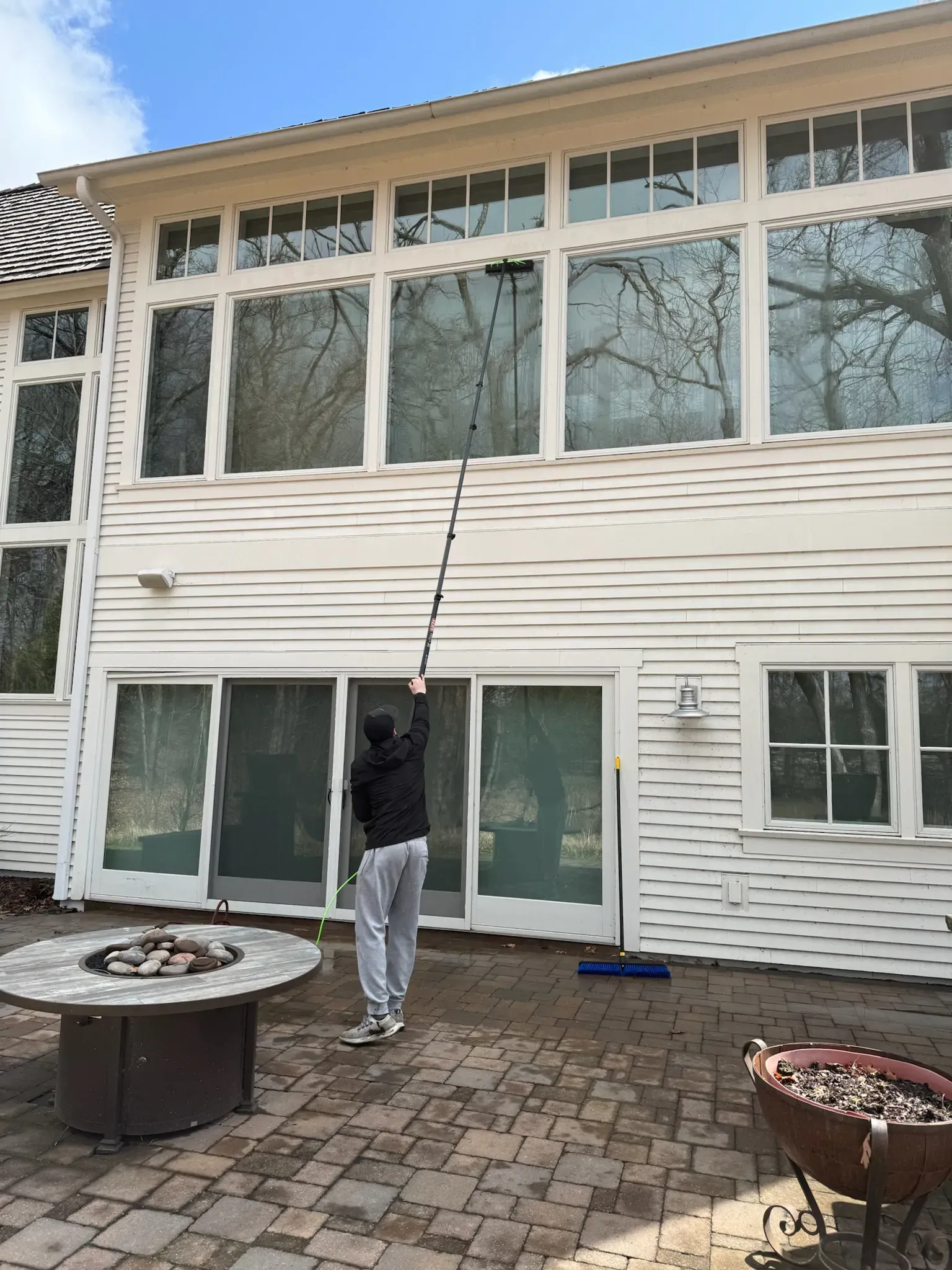 Person cleaning large windows of a white house with an extended pole.