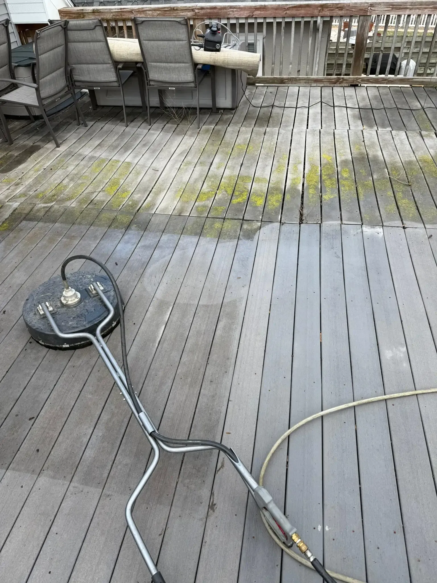 A power washer cleaning a wooden deck, with outdoor furniture in the background.