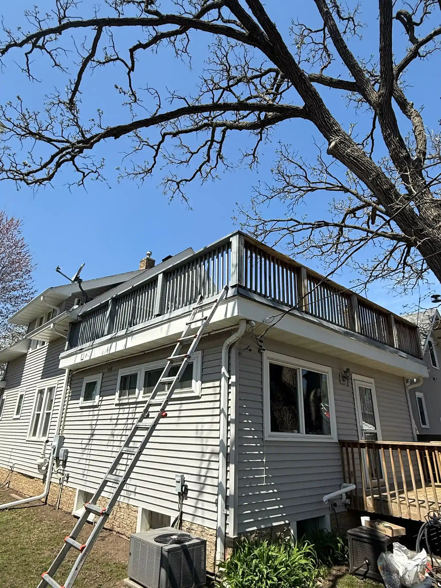 House with a rooftop deck; a ladder leans against the side. Clear blue sky.