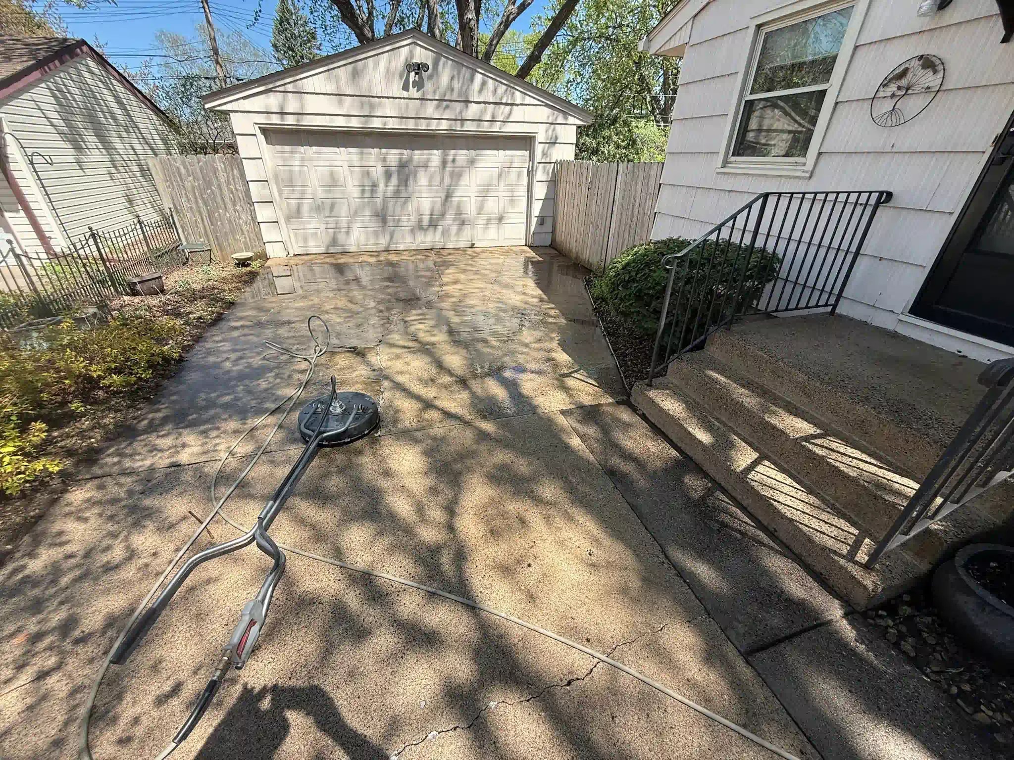 Driveway being power washed, with garage in background, next to house.