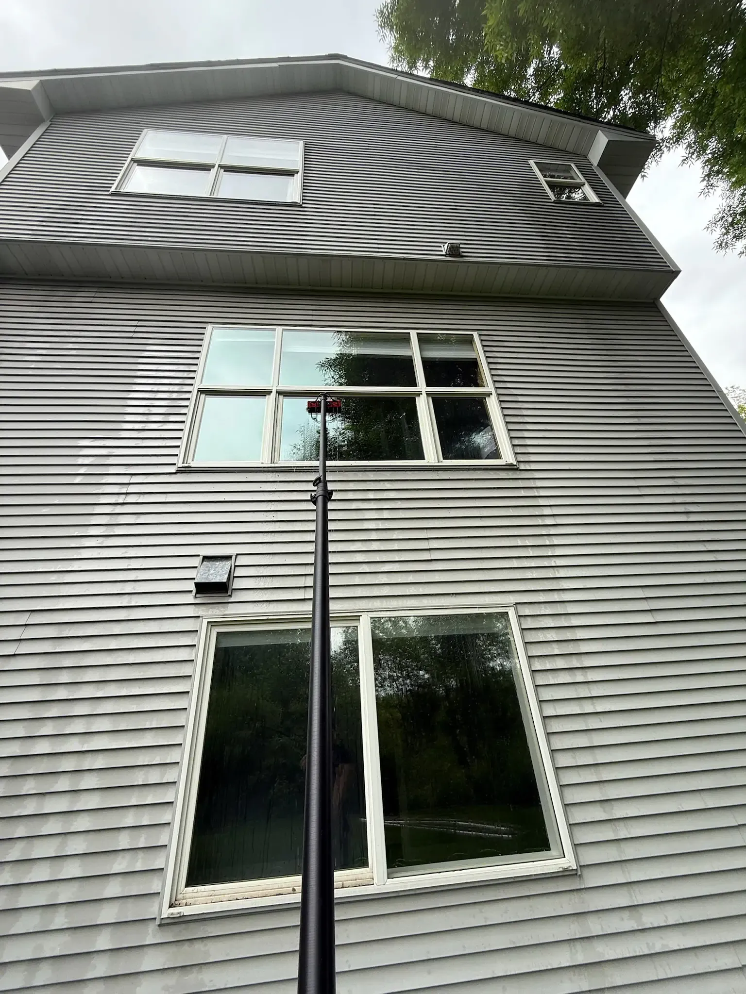 House exterior with a window cleaning pole extended towards windows. Gray siding and swirling black and white pattern on the top level.