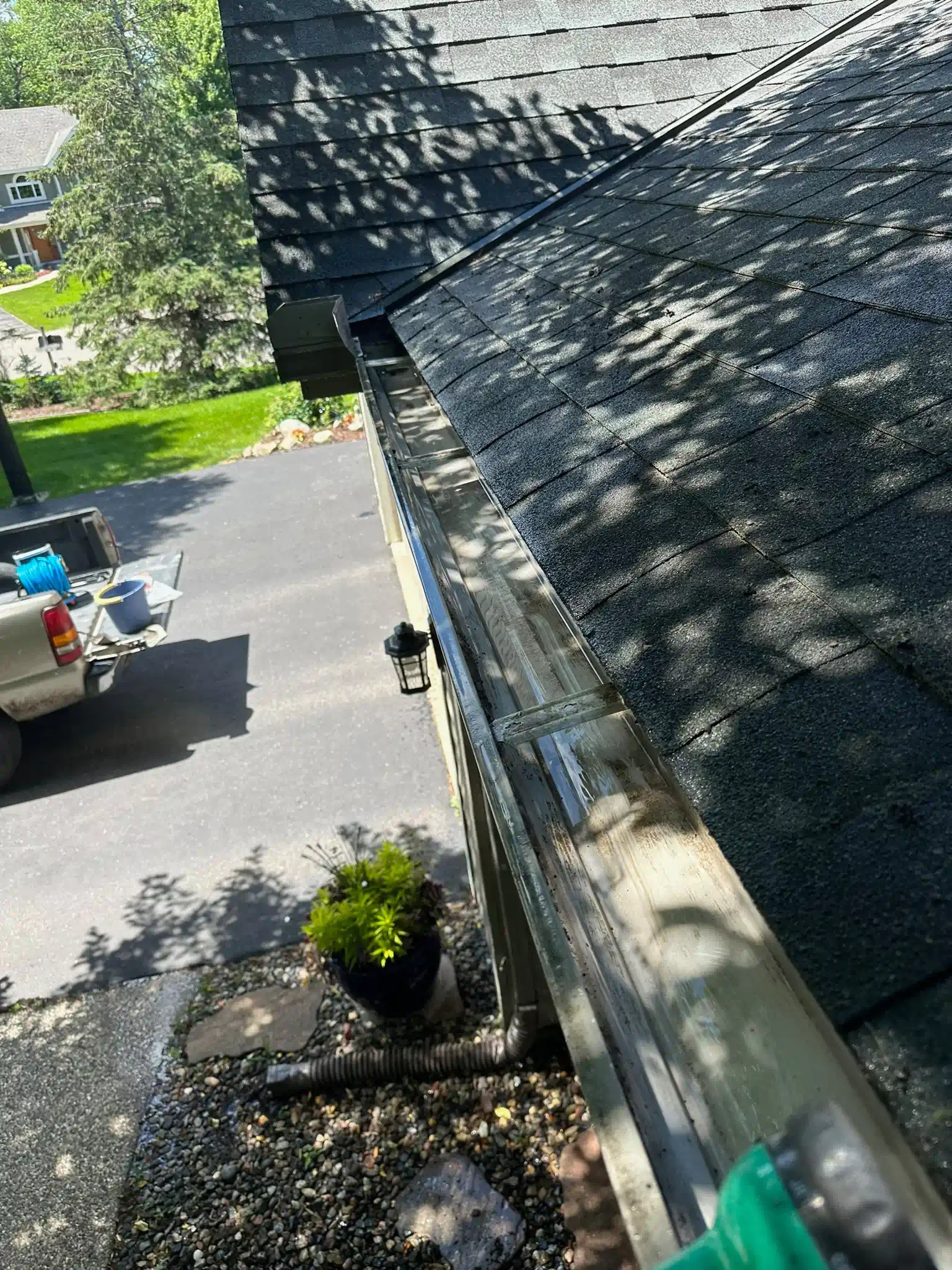 Gutter cleaning on a roof. A person cleans a gutter with a hose. A car and yard are in the background.