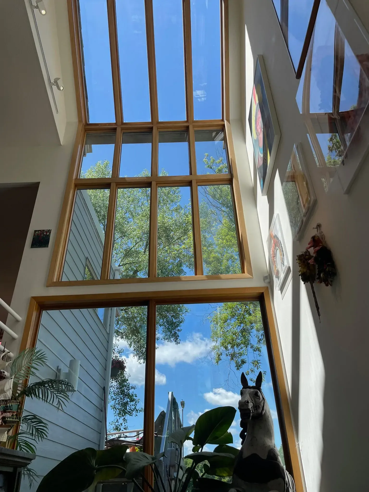 Large windows with wooden frames overlook a blue sky and trees. Sunlight streams into the interior.
