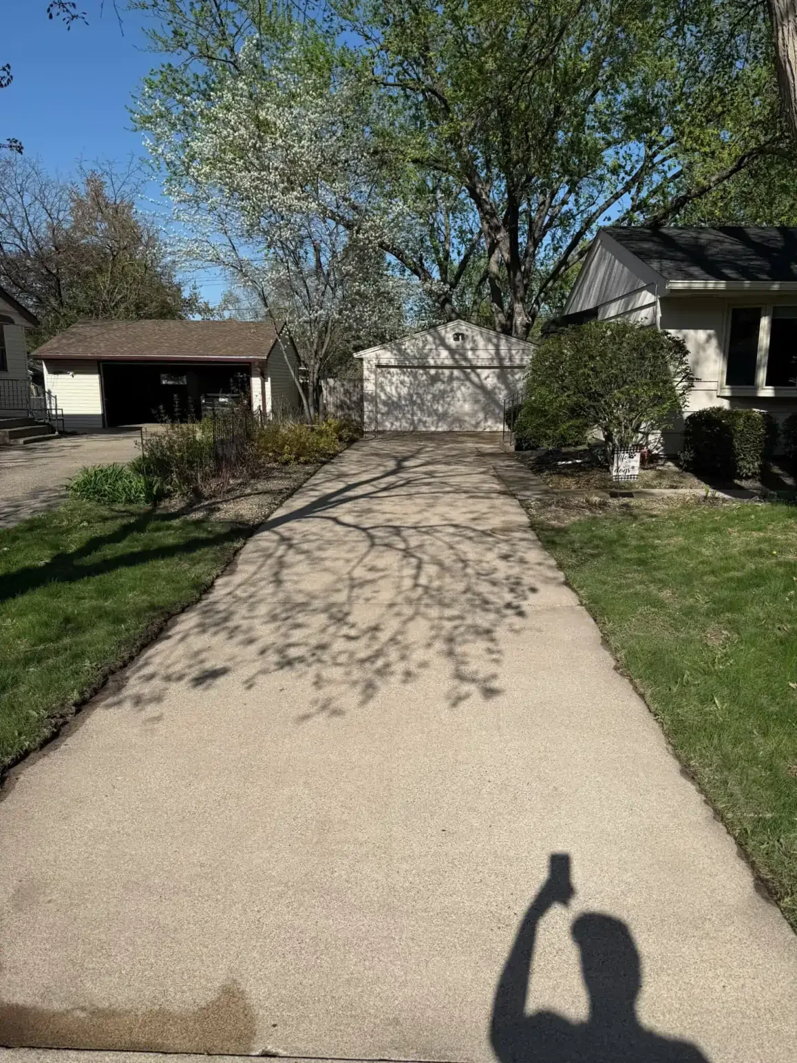 Long driveway with shadow of leaves cast upon it, leading to a garage. Person taking the picture is visible in the foreground.