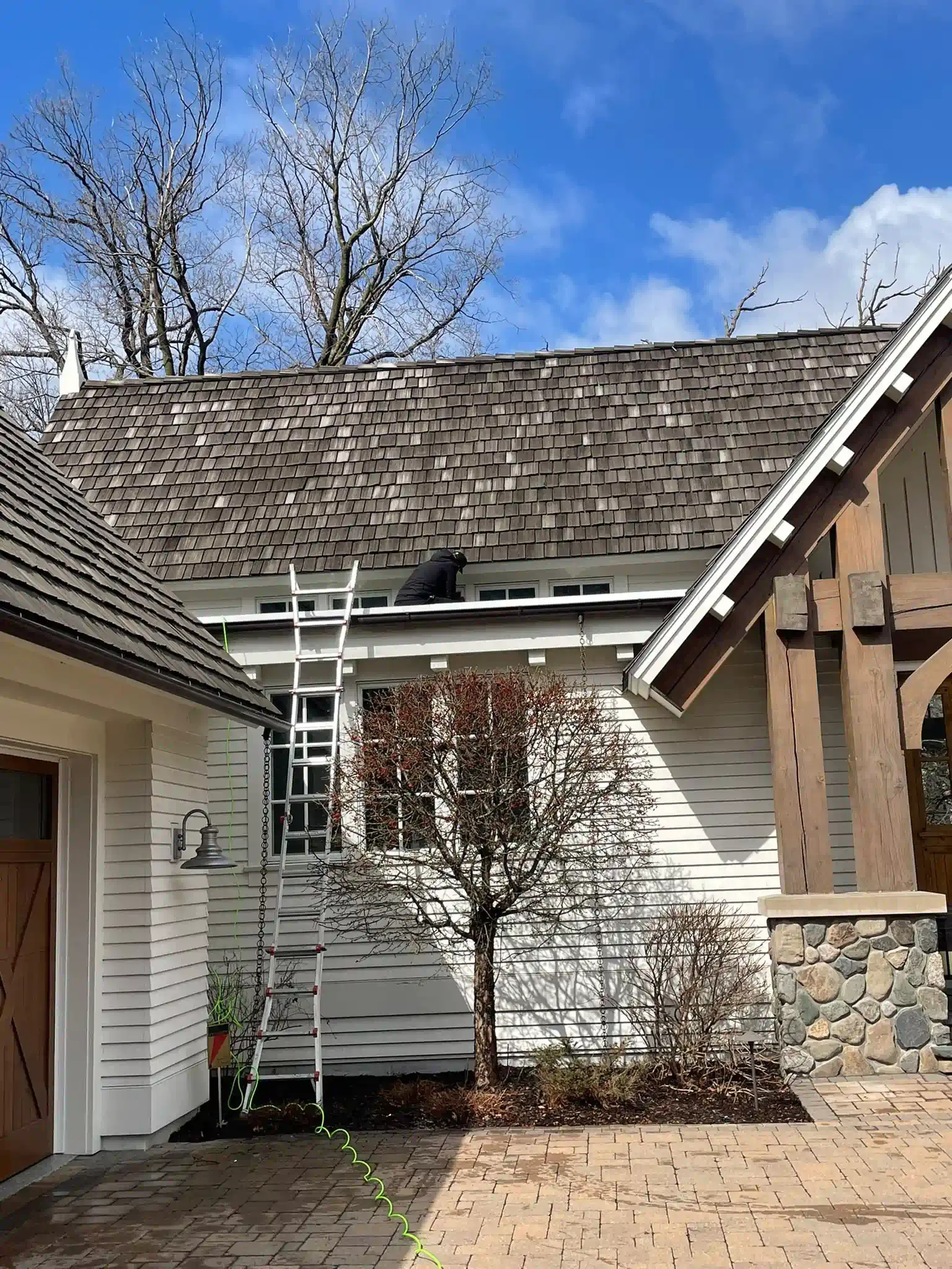 Ladder against a white house with a brown shake roof, under a bright blue sky.
