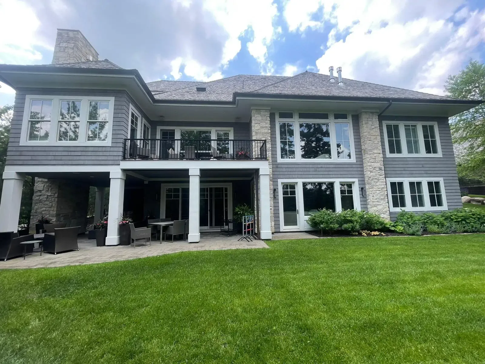 Gray-sided, multi-level house with stone accents, large windows, and a green lawn under a partly cloudy sky.