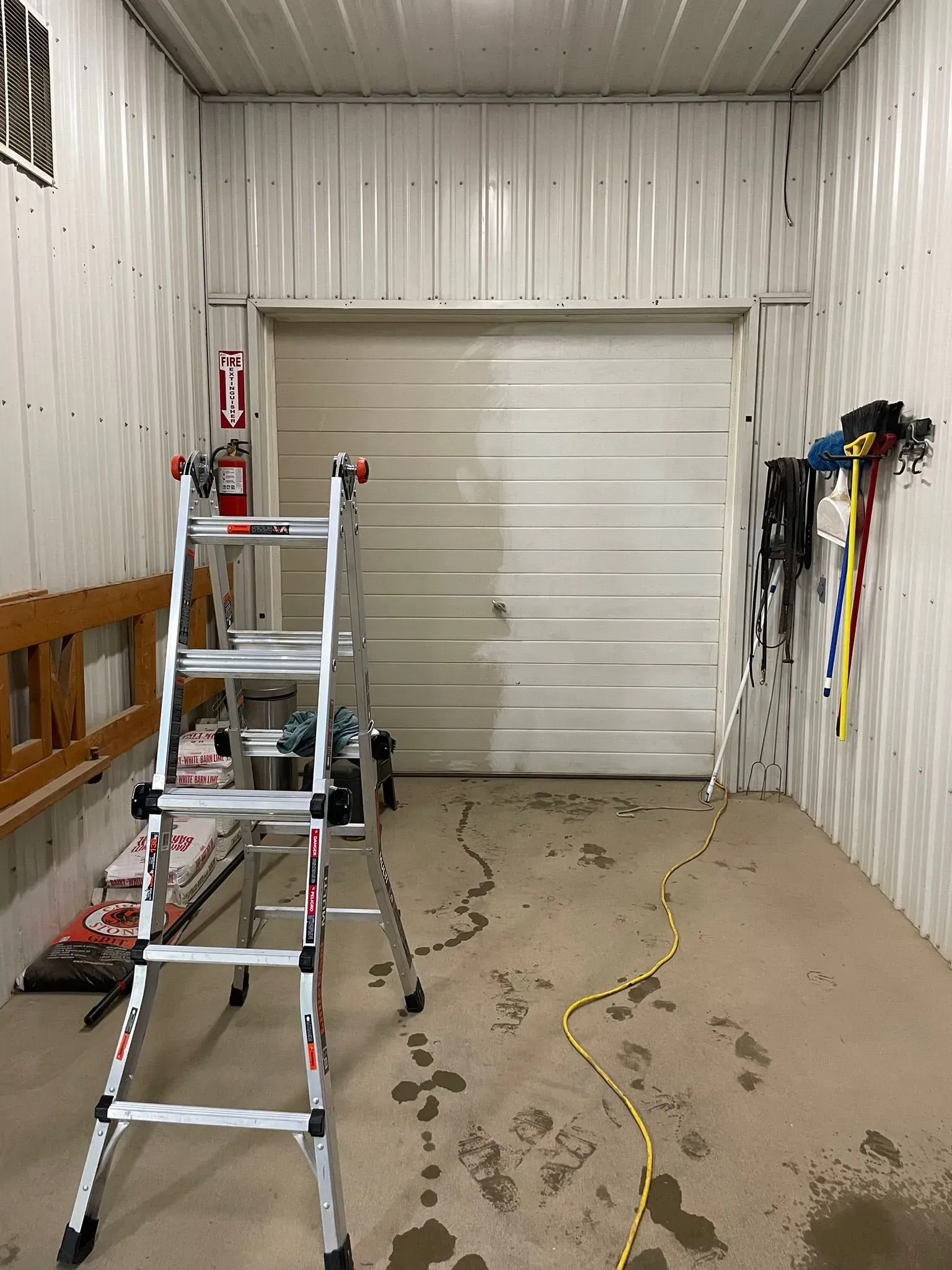 Interior of a garage with a closed overhead door, tools, ladder, and fire extinguisher.