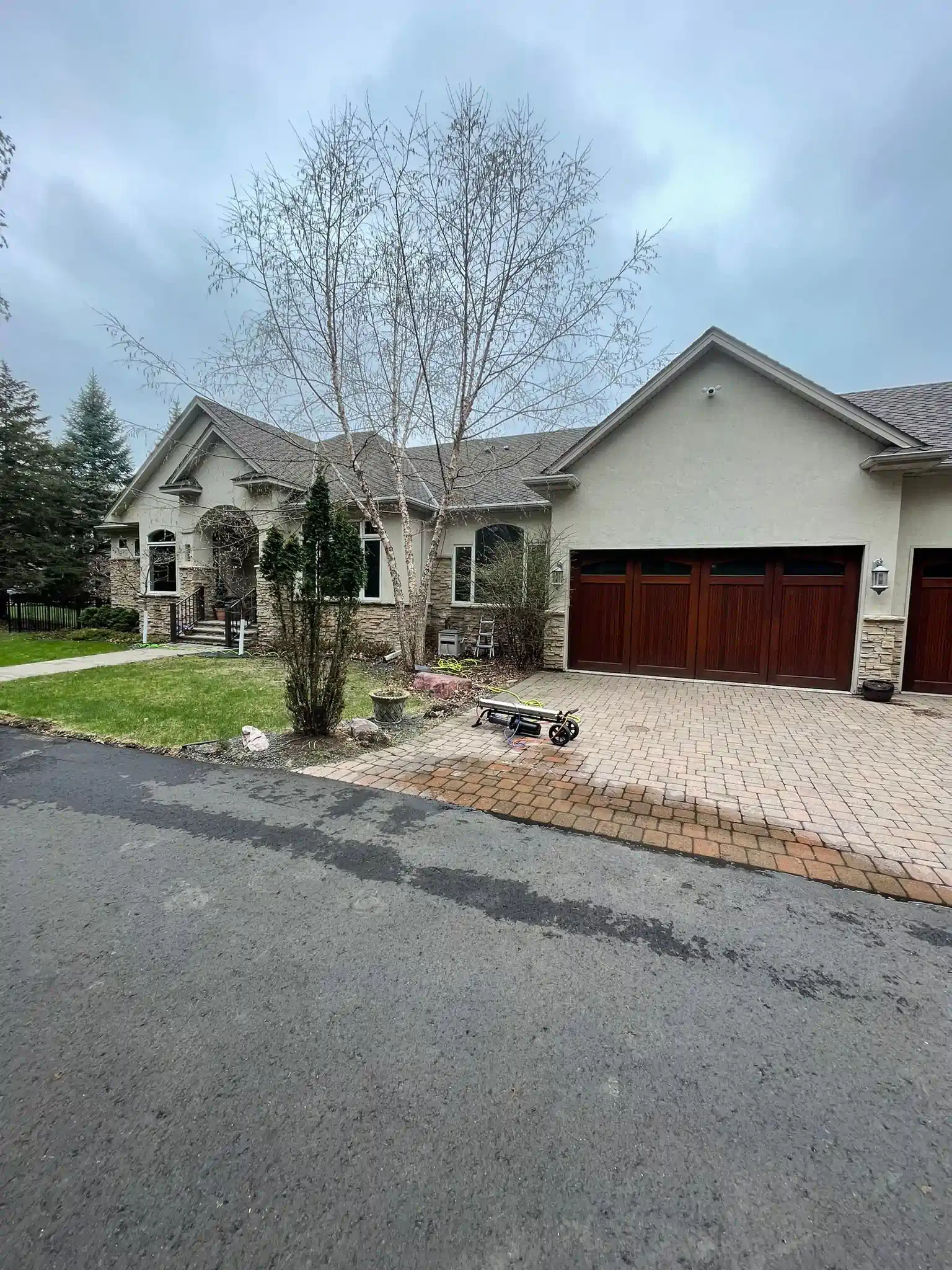 A house with a brick driveway and brown garage doors on an overcast day.