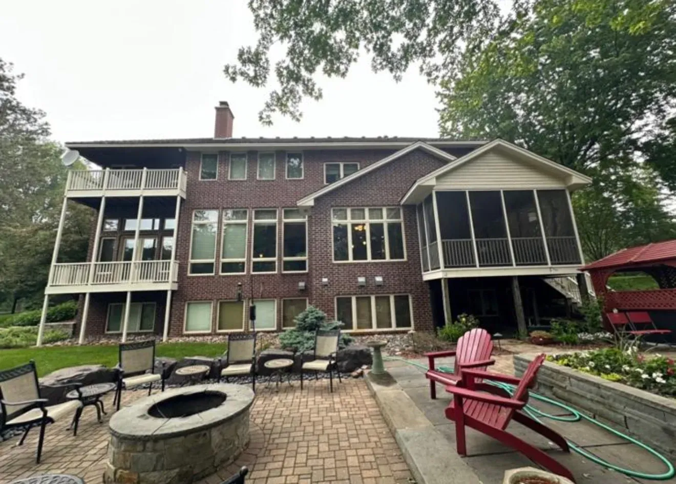 Brick home with two-story screened porch, fire pit, patio furniture, and gazebo in a garden setting.