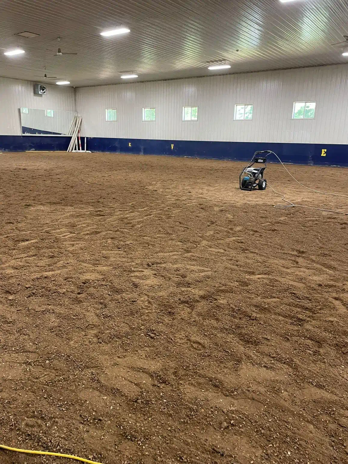 Indoor riding arena with dirt floor, grooming machine, and blue perimeter.