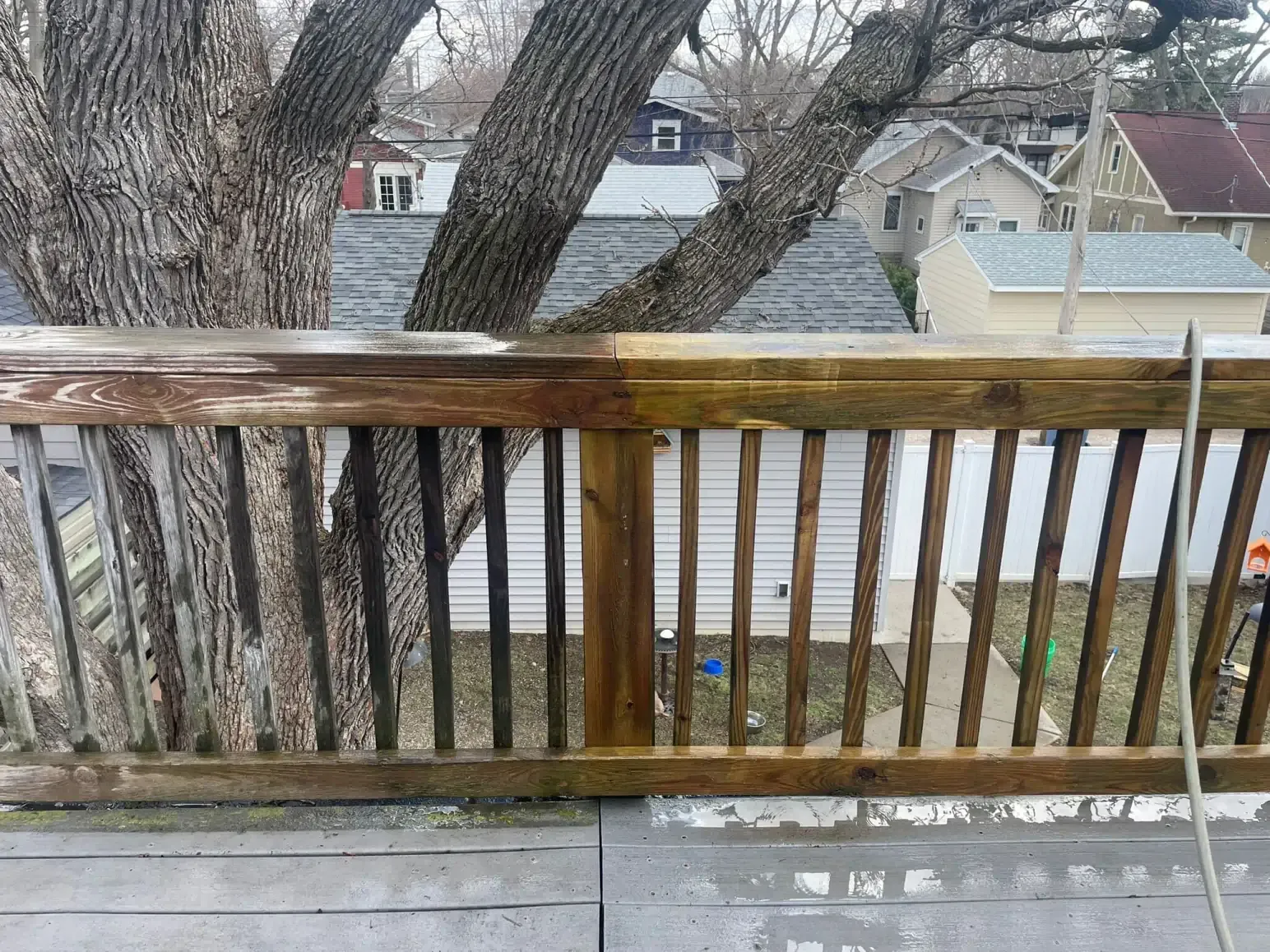 Wooden deck railing, partially cleaned, showing contrast between weathered and refreshed wood.