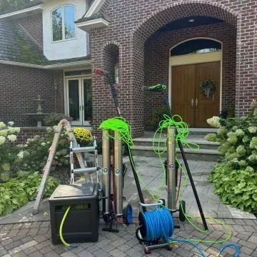 Two-story house with green siding, multiple windows, and a deck, under a blue sky. Landscaping with rock wall and green grass.