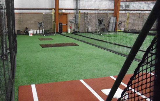 Indoor baseball training facility with turf, cages, and protective netting.