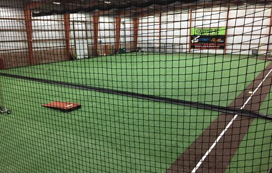 Indoor baseball training facility with turf, cages, and protective netting.