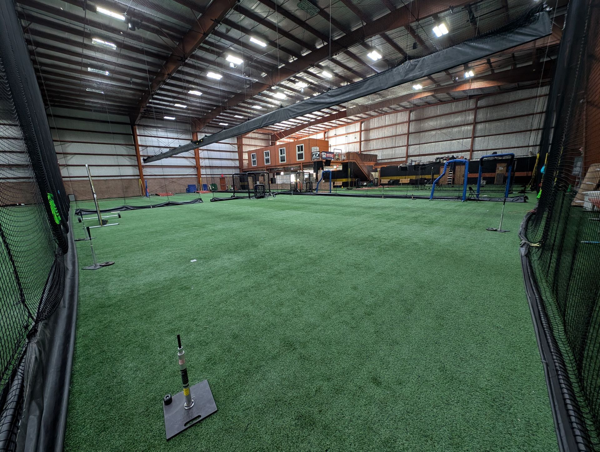 Indoor baseball training facility with turf, cages, and protective netting.